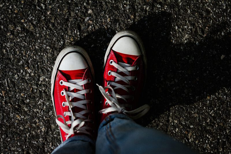 A pair of red converse shoes standing on asphalt