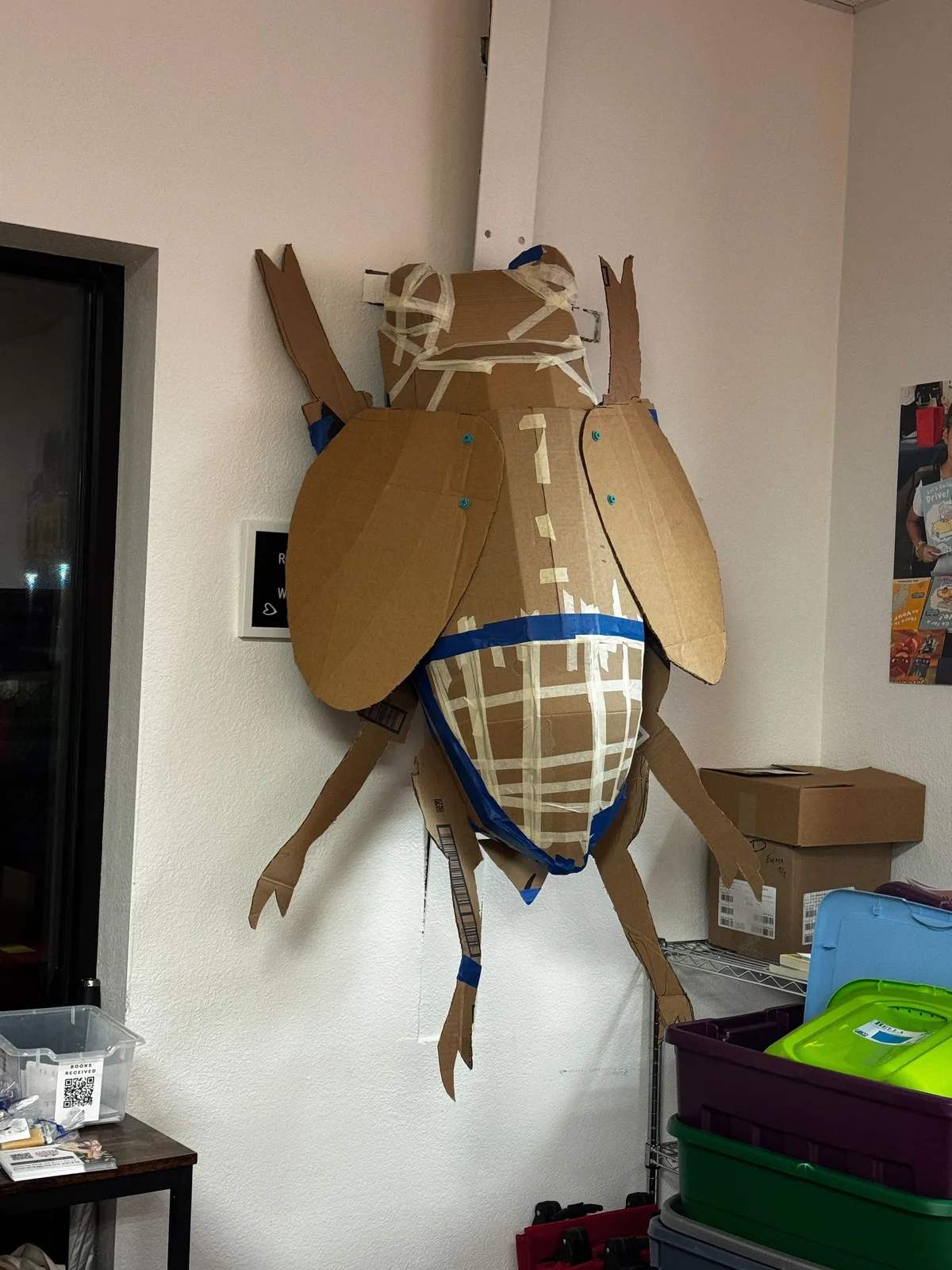 Large bug made out of taped together cardboard hanging on the wall.
