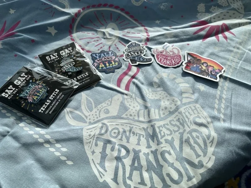 Our bandanas, pins, and sticker swag sold as a fundraiser. A bevy of items supporting the LGBTQIA+ community splashed in sunlight.